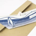 Fischboot aus Papier mit Fischzeichnung, auf braunem Briefumschlag, kreative Papierkunst.