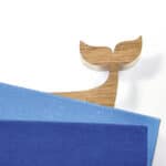 Hölzerner Wal-Schwanz als dekoratives Element auf blauen Büchern, minimalistisches Design, nachhalti.