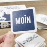 Spielkarte mit dem Wort "MOIN" auf maritime Themenkarten im Hintergrund.
