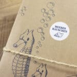Kreative Verpackung mit Seepferdchen-Illustration und Meeresrauschen-Aufkleber.