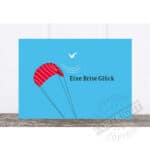 Ein kleine rote Fallschirm mit Vogel und Wasserwellen, Text: Eine Brise Glück, Glücksmoment, Luftfah.