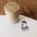 Hölzerner Stempel auf weißem Papier mit handgezeichneter Ente in Pullover, kreative Drucktechnik.
