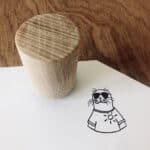 Hölzerner Stempel auf weißem Papier mit Katzenzeichnung in Sonnenbrille und T-Shirt.