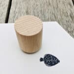 Ein Holzstempel auf weißem Papier mit Fischzeichnung, auf einem Holztisch.