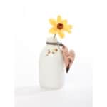 Ein weißes Milchflaschen-Design mit gelber Blume und Herzanhänger, minimalistisch und dekorativ.