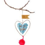 Hängendes Herz mit "mit viel Liebe" Schrift, goldene Flagge, rotem Pompon, dekoratives Naturmaterial.