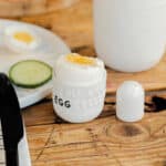 Frühstücksei in Eierbecher mit Salzstreuer, Gurkenscheiben und Kaffee auf Holz Tisch, Frühstück, Ei,.