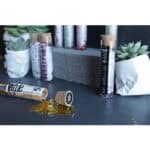 Hochwertige CBD-Produkte in Glasröhrchen mit Goldstaub, auf dunklem Tisch mit Sukkulenten und Bücher.