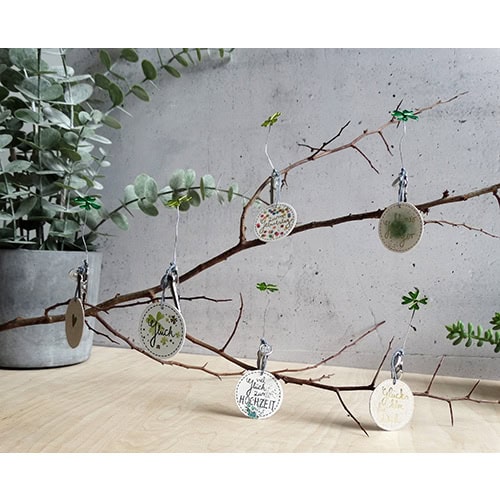 Dekorative Zweig mit handgemachten Weihnachtsornamenten und grünen Pflanzen.