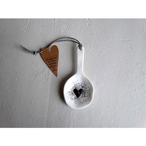Dekorative weiße Löffel mit Herzmotiv und Anhänger gegen graue Wand.