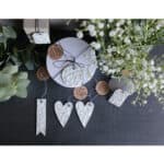 Hochzeitliche Dekoration mit weißen Herz- und Anhänger-Elementen, Blumen und Naturmaterialien.