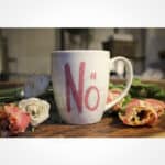Becher mit "No" Schriftzug und Blumen auf Holzoberfläche, gemütliche Atmosphäre.