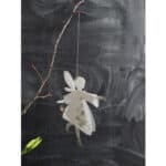 Ein niedliches Engel-Mobile aus Papier mit Blumenmuster, hängt an einem Zweig vor einer dunklen Wand.