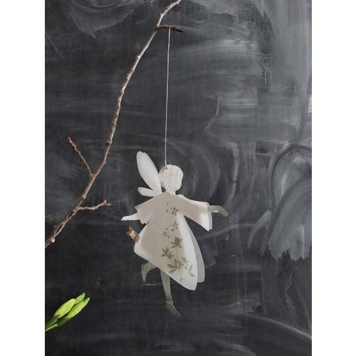 Ein niedliches Engel-Mobile aus Papier mit Blumenmuster, hängt an einem Zweig vor einer dunklen Wand.