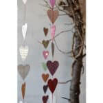 Bunte Papierherzen hängen an einer Schnur vor einem Baumstamm, symbolisieren Liebe und Zuneigung.