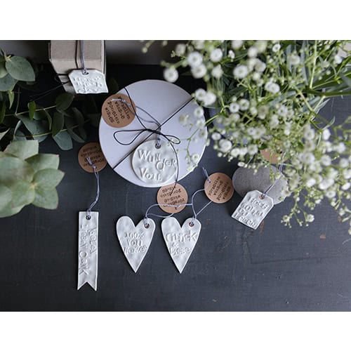 Hochzeitliche Dekoration mit weißen Herz- und Anhänger-Elementen, Blumen und Naturmaterialien.