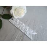 Hochwertiges weißes Kerzengeschenk mit "Willkommen" Schriftzug und weißer Rose auf grauem Hintergrun.