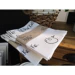 Handgemachte T-Shirts mit kreativen Designs und Texten, auf einem Holzschreibtisch liegend.