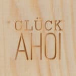 Hölzernes Holzschild mit dem Wort "Glück" und "Ahoi" in dekorativem Design, maritime und glücksbring.
