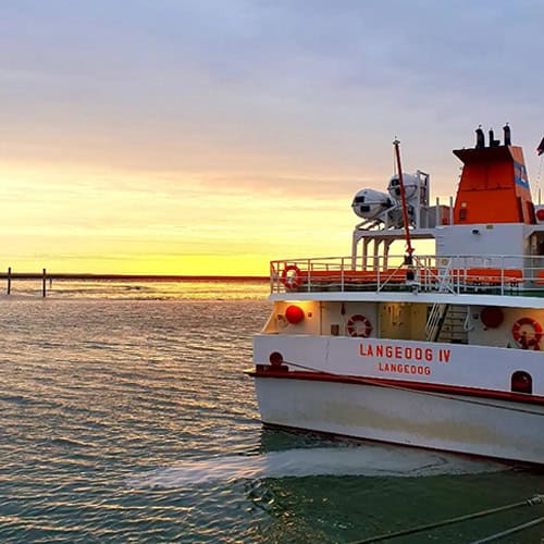 Ein Frachtschiff bei Sonnenuntergang im Hafen, mit Blick auf den Horizont und ruhiges Wasser.