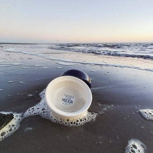 Ein Eimer am Strand mit Wasser und Seifenblasen, Blick auf das Meer bei Sonnenuntergang.