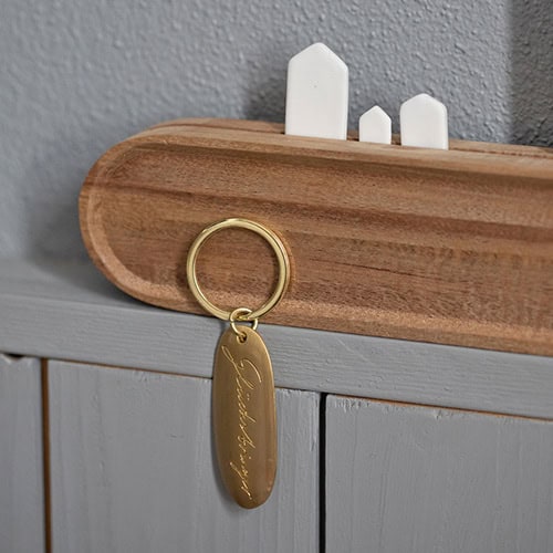 Schlüsselanhänger mit Gravur an Holzschrank, minimalistisches Design.