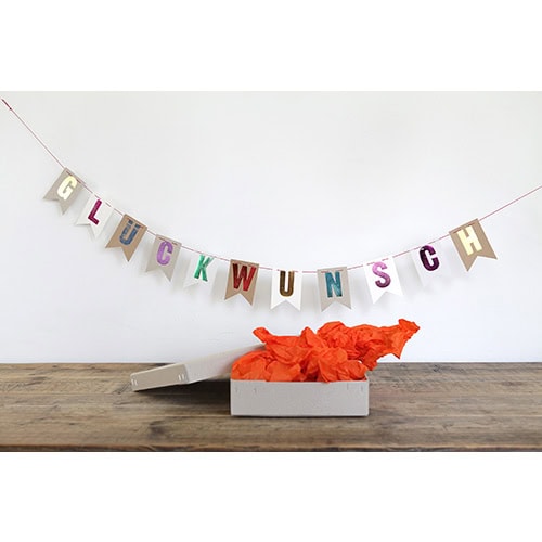 Willkommensdekoration mit bunten Buchstaben und Geschenkbox auf Holzoberfläche, festliche Atmosphäre.