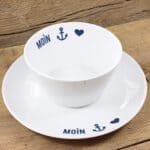 Mikrowellengeeignete weiße Tasse mit Anker- und Herzmotiven, "MOIN" Schriftzug, auf Holzuntergrund.