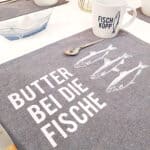 Dekorativer Tischläufer mit Fischmotiven und Spruch "Butter bei die Fische" in modernem Design.