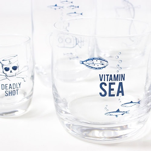 Glas mit "Vitamin Sea" Aufdruck und Meeresmotiven, transparentes Wasser, kreative Meeresillustration.