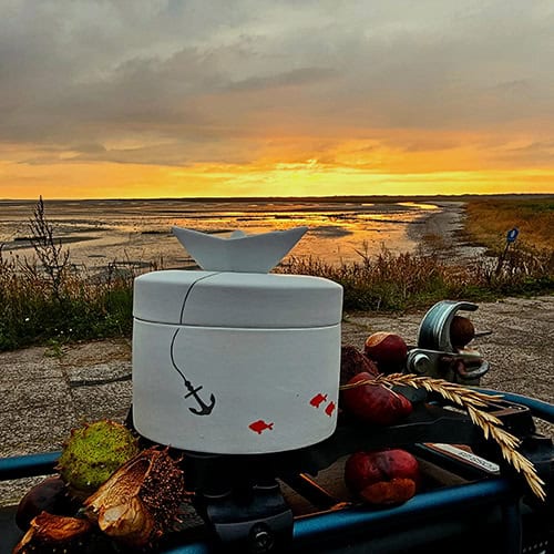 Hübsche maritime Dekoration mit Anker und Fischen am Wasser bei Sonnenuntergang.