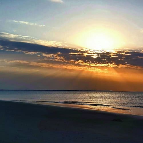 Ein ruhiger Sonnenuntergang über dem Meer mit sanften Wellen und einem klaren Himmel.