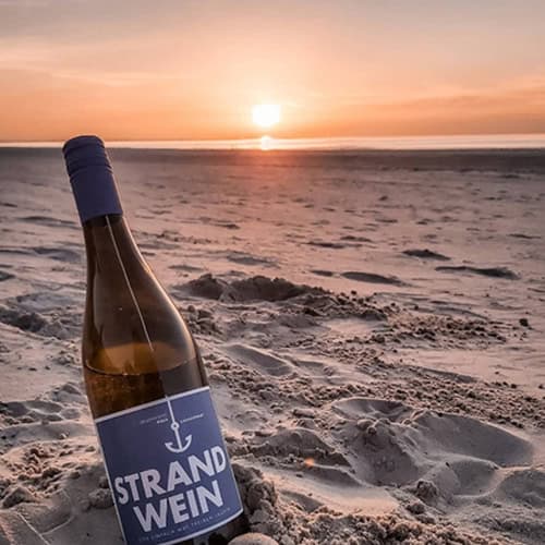 Ein Flasche Strandwein am Sandstrand bei Sonnenuntergang, ideal für Weinliebhaber und Urlaubsstimmun.