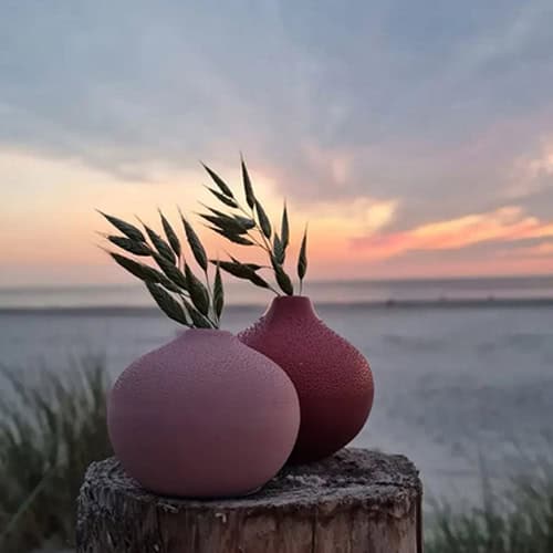 Elegante Keramikvasen mit Gräsern am Strand bei Sonnenuntergang, stilvolle Dekoration für Zuhause.