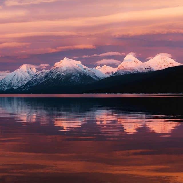 Atemberaubende Berglandschaft mit schneebedeckten Gipfeln bei Sonnenuntergang, spiegelt sich im ruhi.