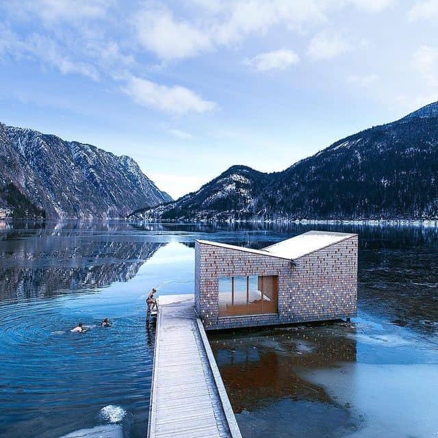 Modernes Haus auf dem Wasser in norwegischer Fjordlandschaft mit Bergen im Hintergrund.
