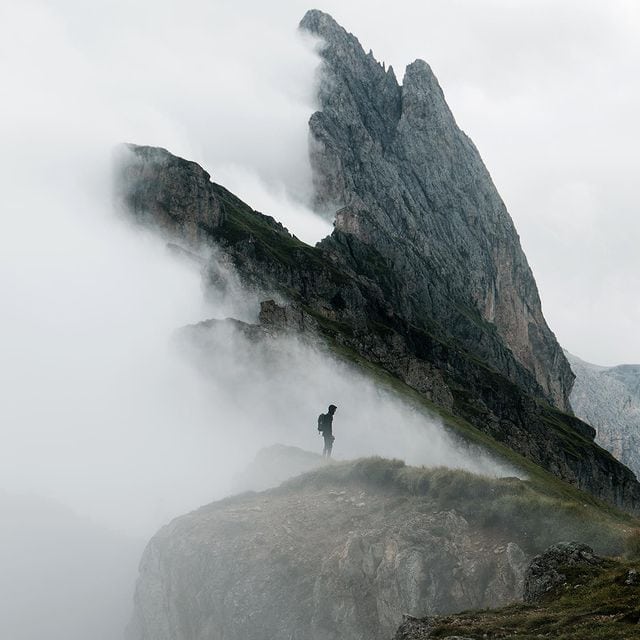 Bergsteiger auf schmalem Grat in den Bergen, umgeben von Nebel und hohen Felsen.