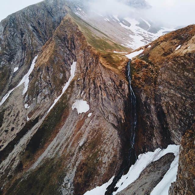 Atemberaubende Berglandschaft mit Wasserfall und Schneefeldern in den Alpen.