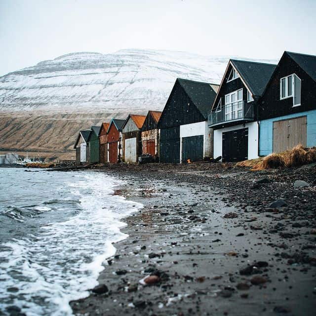 Bunte Fischerhäuser am Strand in Island mit Blick auf Berge im Hintergrund.