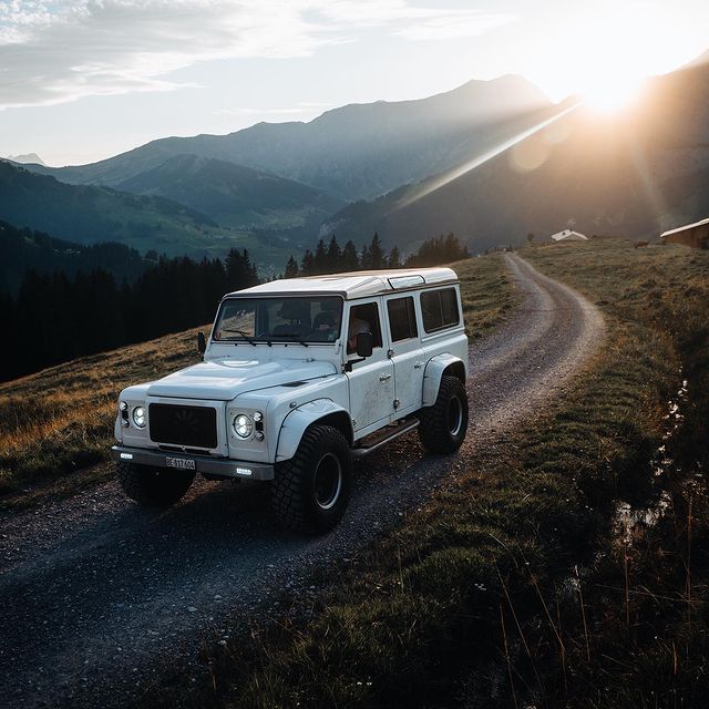 Geländewagen auf unbefestigter Bergstraße bei Sonnenuntergang, umgeben von Bergen und Natur, ideal f.