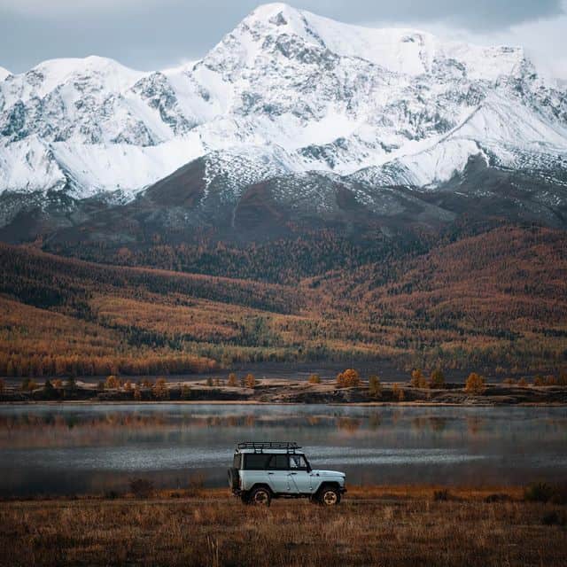 Berglandschaft mit verschneiten Gipfeln, See und einem Auto im Vordergrund, ideal für Natur- und Abe.