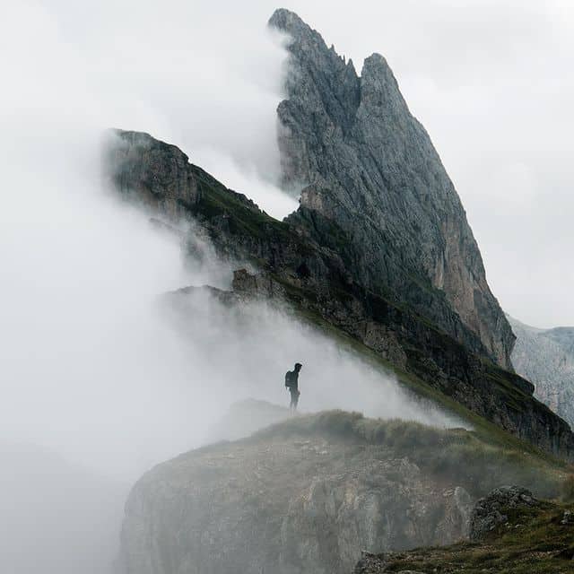 Bergsteiger auf nebligem Gipfel mit beeindruckender Felsformation.