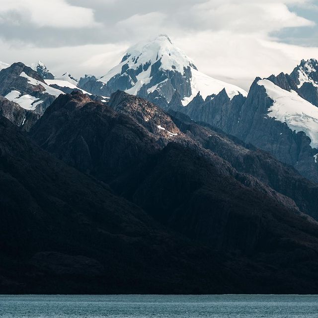 Alpen-Gipfel mit Gletscher, beeindruckende Berglandschaft und ruhiger See im Vordergrund.