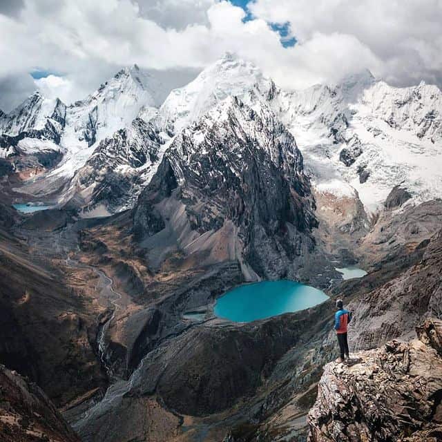 Wanderer auf Felsvorsprung mit Blick auf Himalaya-Gipfel und Bergsee.