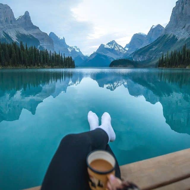 Blick auf einen ruhigen Gletschersee in den Rocky Mountains, umgeben von hohen Bergen und Tannenwäld.