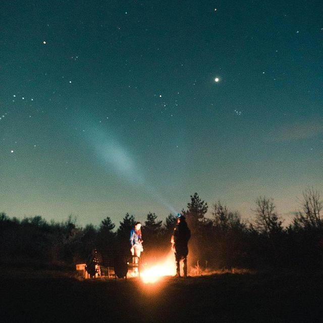 Sternenhimmel und Lagerfeuer mit Menschen in der Natur, nächtliche Outdoor-Aktivität, Sternschnuppen.
