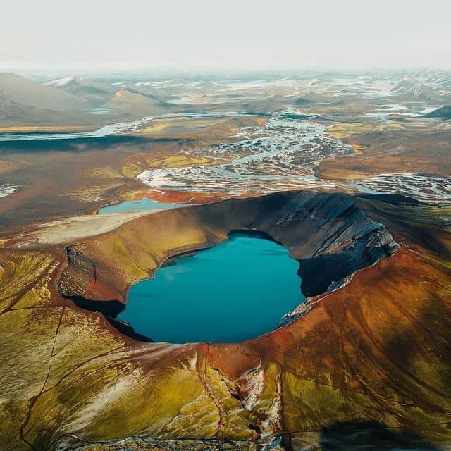 Vulkankrater mit blauem See, umgeben von grünen und braunen Hängen, in Island.