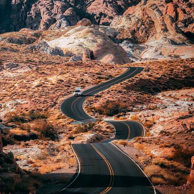Wüstenstraße in Arizona mit kurviger Straße und roten Felsen im Hintergrund.