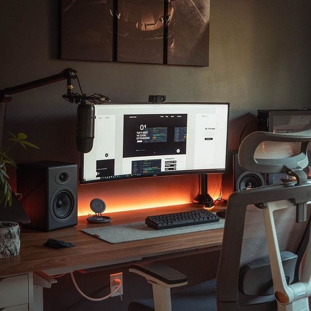 Arbeitsplatz mit großem Monitor, Lautsprechern und Mikrofon in stilvollem Home-Office.
