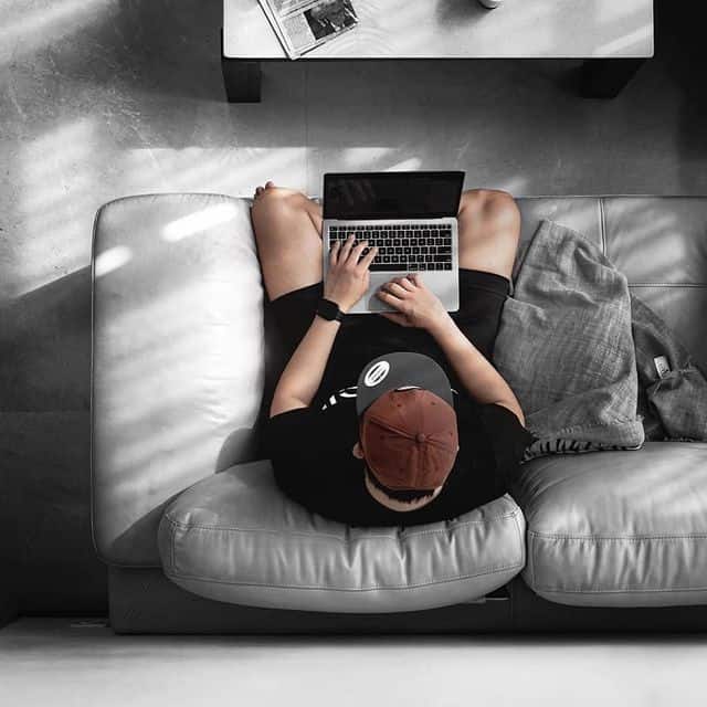 Junge Person mit Laptop auf Sofa, entspannt zu Hause, modernes Arbeiten.